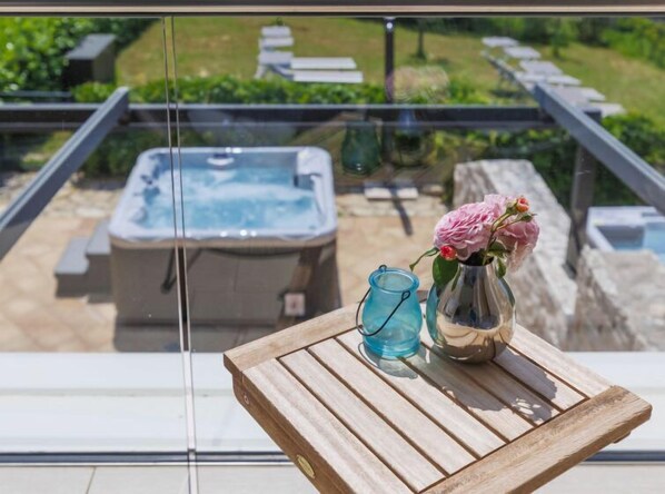 A wooden table with a vase of flowers and a glass on a balcony overlooking a hot tub and outdoor seating area.