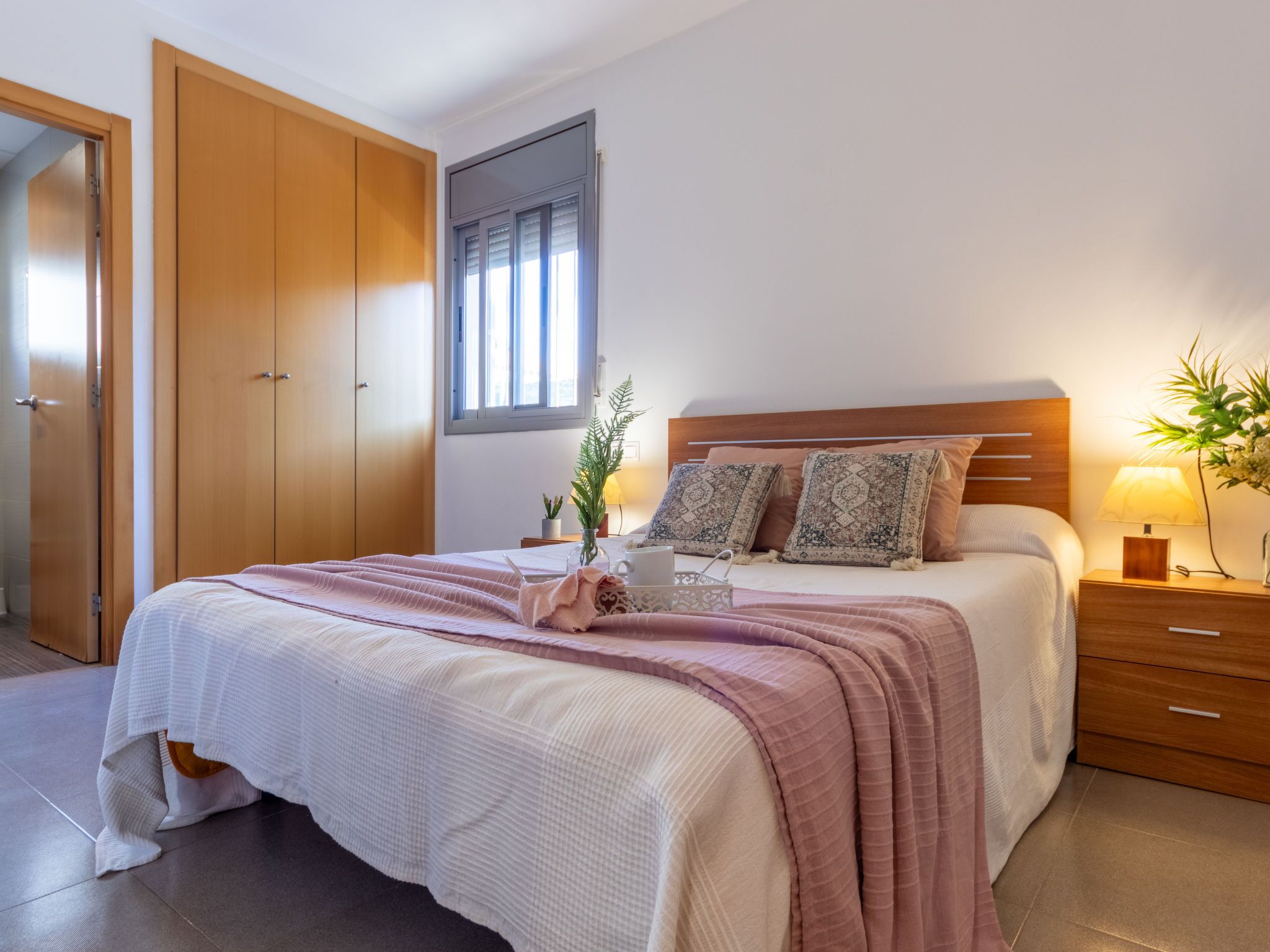 A bedroom with a bed, bedside table, lamp, and a window with blinds.