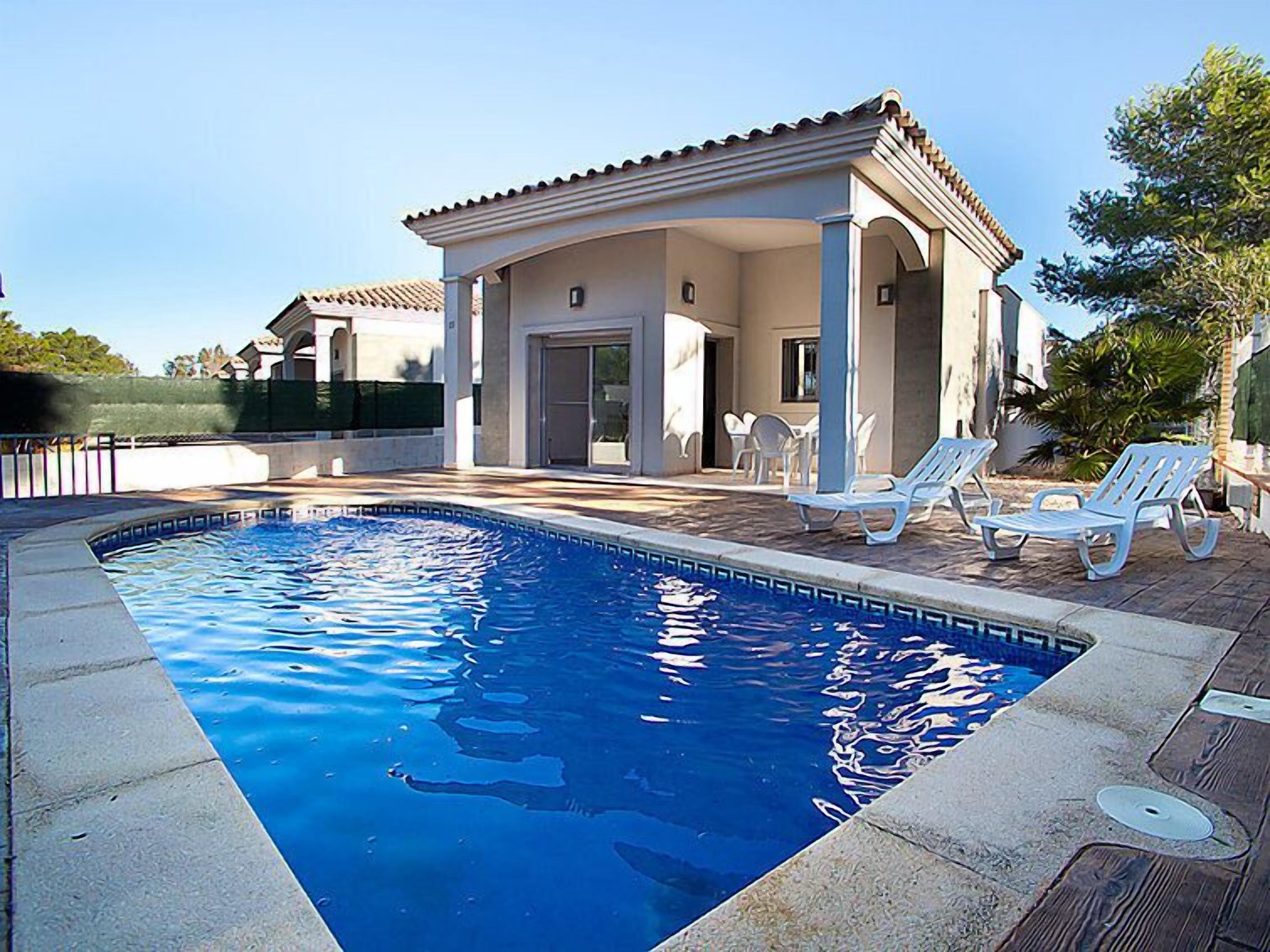 A swimming pool with a tiled deck, white lounge chairs, and a covered patio area.