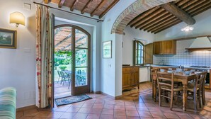 Une cuisine spacieuse avec des meubles en bois, une table à manger et une vue sur un jardin, accessible par une porte ouverte.