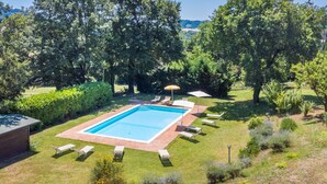 Une piscine rectangulaire bordée d’une terrasse carrelée, entourée d’une pelouse où se trouvent plusieurs chaises longues et des parasols.
