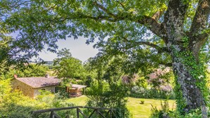 Un bâtiment rustique en pierre, doté d’un toit en tuiles, entouré d’une végétation luxuriante et d’un pont en bois.