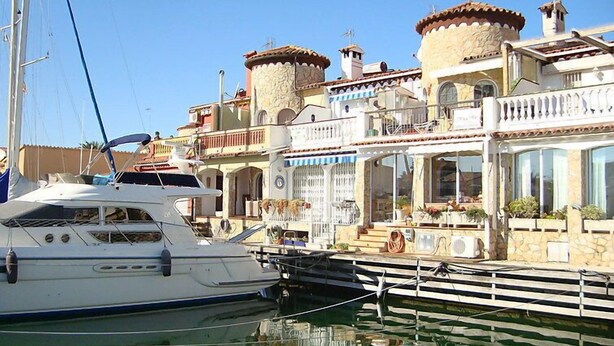 Un puerto deportivo con un yate blanco amarrado, un edificio con varios balcones y un cielo azul despejado.