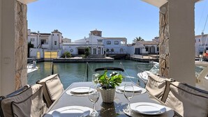Mesa con vajilla, vasos y una planta en maceta, con vista a un puerto deportivo con barcos y edificios.