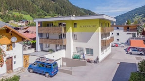 Ein mehrstöckiges Gebäude mit der Aufschrift "ALPENROSE" an der Fassade, umgeben von einer gebirgigen Landschaft.