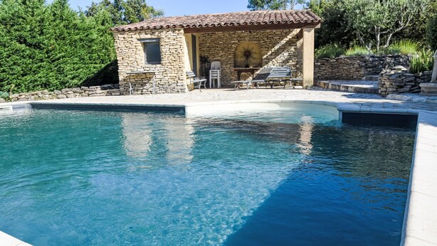 Une piscine aux murs en pierre et un petit bâtiment en pierre doté d’une fenêtre et d’une porte.
