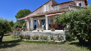Une maison à deux étages avec une façade en pierre, une véranda couverte avec des meubles d’extérieur et un mur de pierre qui entoure la propriété.