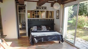 Une chambre à coucher avec un lit, une table en bois et une vue sur un jardin, accessible par une porte-fenêtre coulissante.