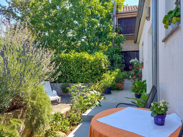 A patio with a table, surrounded by potted plants and a variety of greenery.