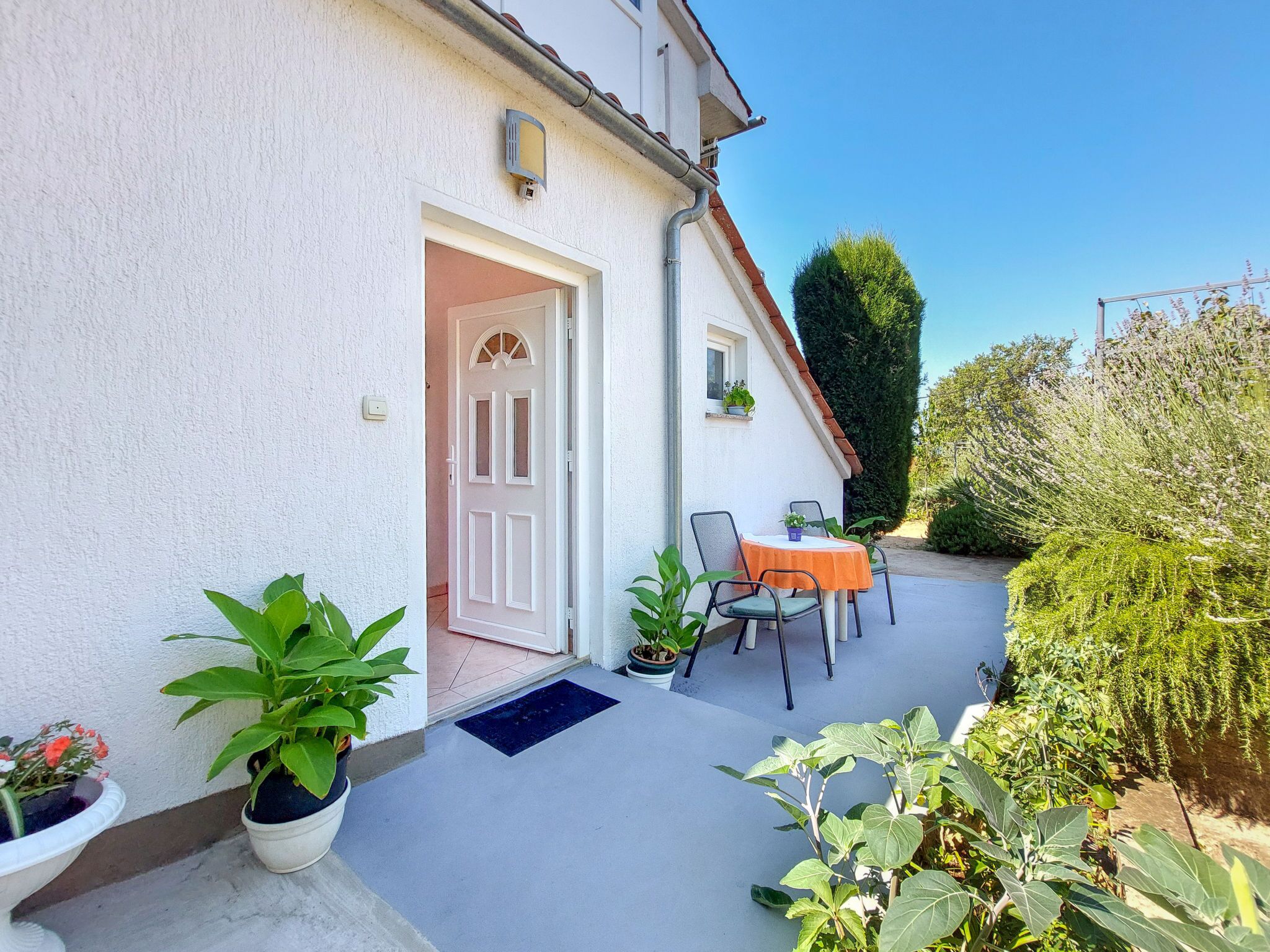 A house with a white exterior, a door, and a small patio area with a table and chairs.