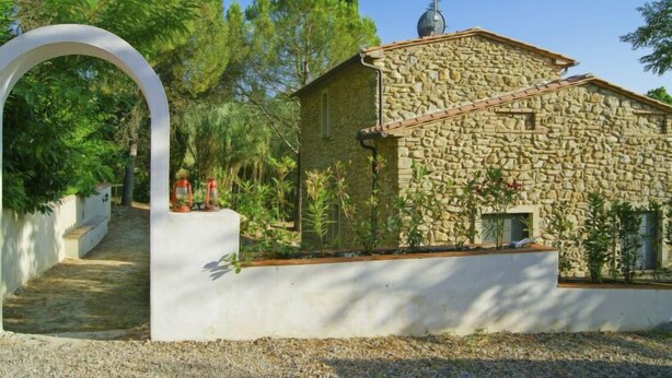 A stone building with a sloped roof, a chimney, and a small garden area with plants and a pathway leading to an archway. - Villa Sofia by Interhome (Volterra)