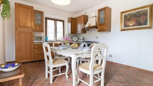 A kitchen with wooden cabinets, a white dining table with chairs, a hanging light fixture, and a painting on the wall. - Villa Sofia by Interhome (Volterra)