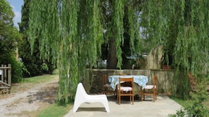 A patio with a table and chairs, surrounded by a stone wall and weeping willow trees. - Villa Sofia by Interhome (Volterra)