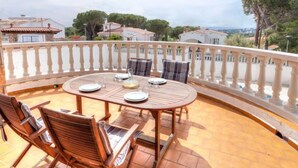 A round wooden table with chairs on a balcony with a white balustrade, overlooking a residential area with houses and trees. - Afrodita by Interhome (L'Escala)