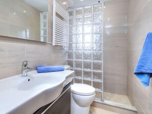 A bathroom with a white sink, mirror, and toilet. There is a shower area with a glass door and a blue towel hanging on the wall. - Afrodita by Interhome (L'Escala)