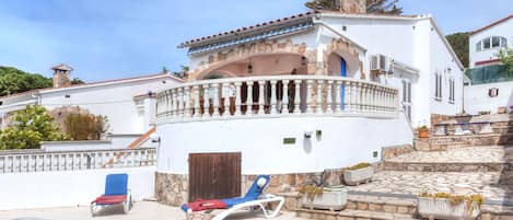 A white villa with a swimming pool, a stone staircase, and a balcony with a white balustrade.