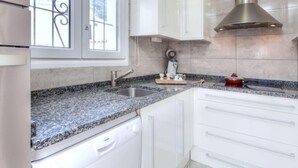 A kitchen with white cabinets, a stainless steel range hood, a granite countertop, and a window with a blue valance. - Afrodita by Interhome (L'Escala)