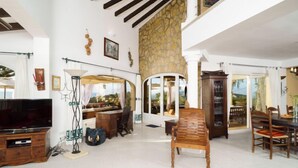 A spacious living room with a large TV, a wooden bench, and a stone wall. - Bellevue by Interhome (Jávea)