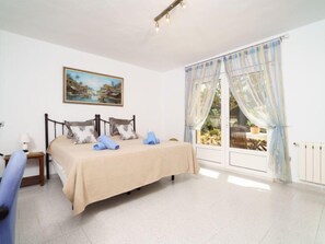 Een slaapkamer met een bed, een nachtkastje, een lamp, een schilderij en een raam met gordijnen.