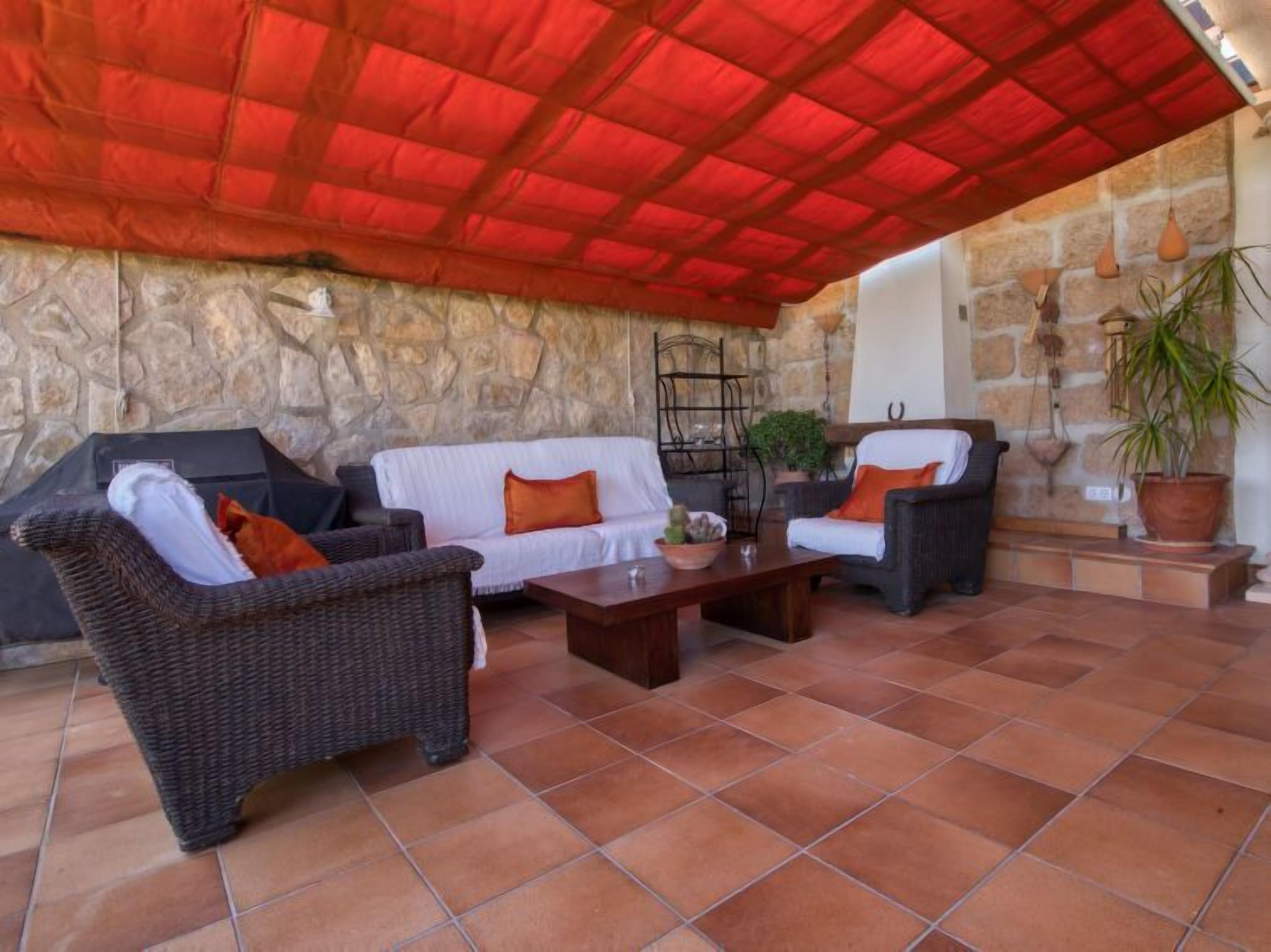 An outdoor patio with stone walls, wicker furniture, and a red roof.