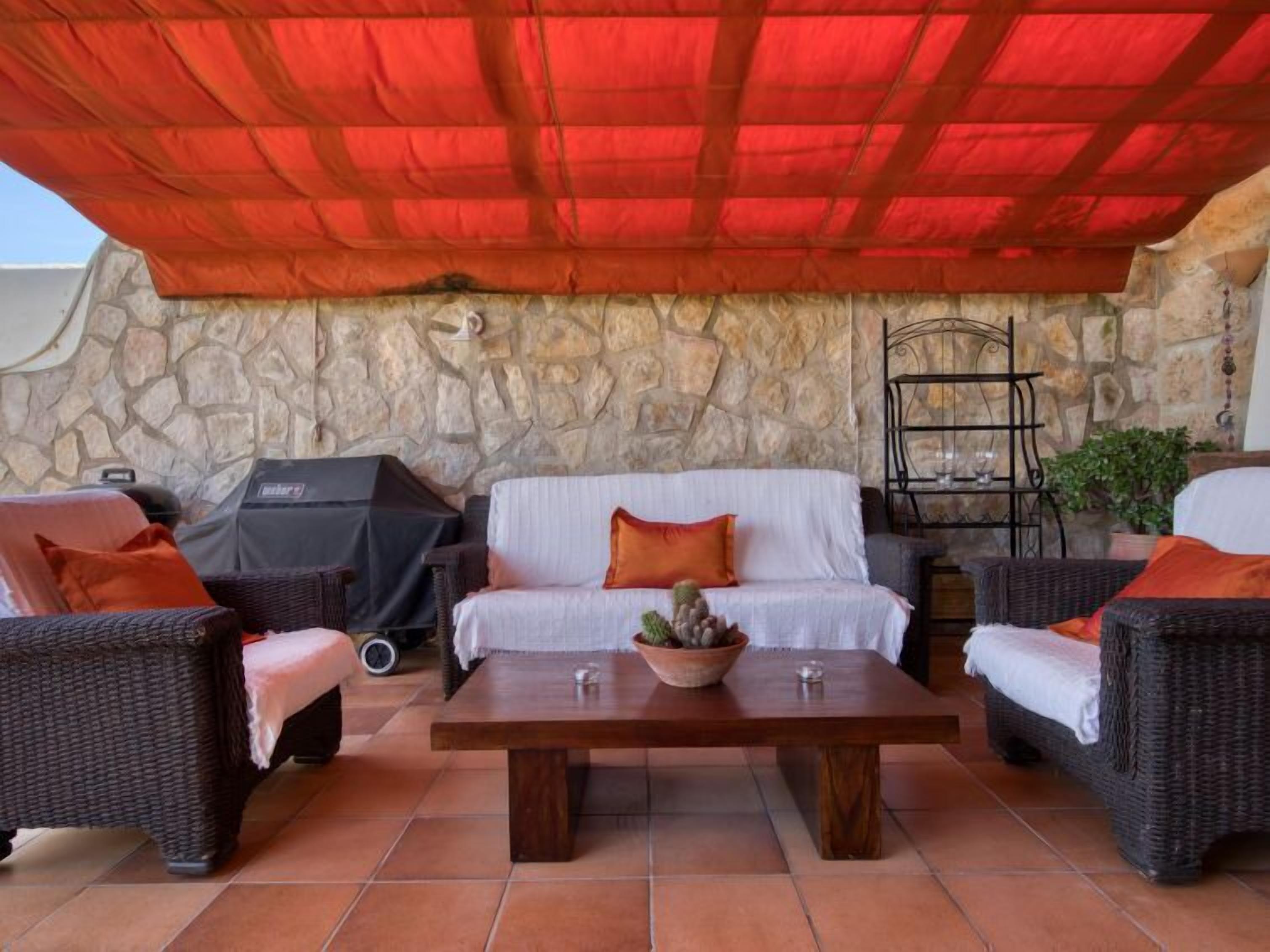 Une terrasse extérieure avec des meubles en osier, un mur en pierre et un auvent rouge.