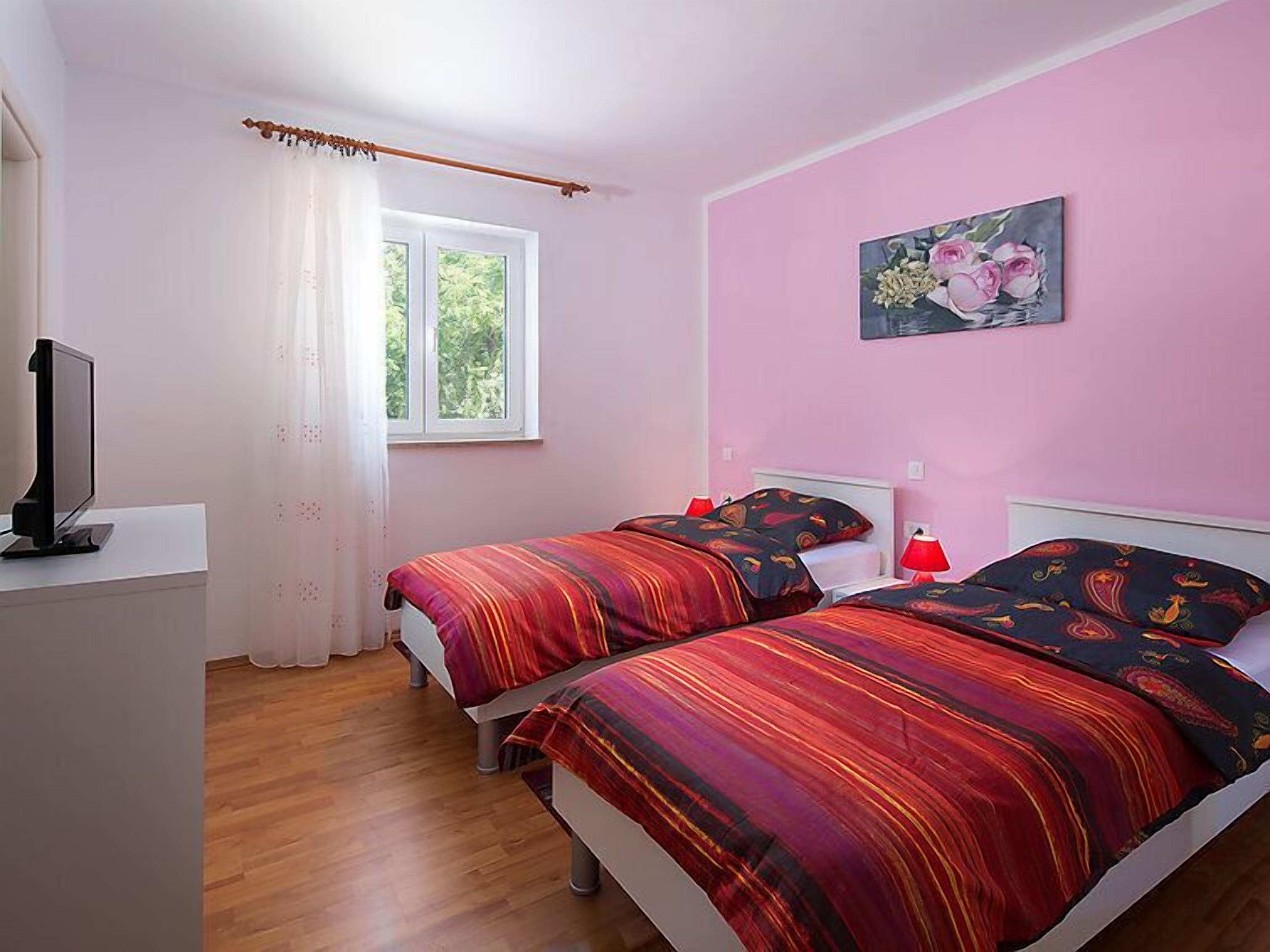 Una habitació amb dos llits, una finestra amb cortines, un quadre a la paret i un escriptori amb un ordinador.