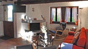 Uma sala de estar com lareira, um sofá, uma poltrona e uma mesa.