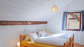 Quarto com cama de madeira, mesa de cabeceira, luminária, luz pendente e janela com cortinas.