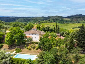A villa with a swimming pool surrounded by lush greenery and vineyards in the background.