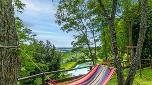 Un hamac tendu entre deux arbres, offrant une vue sur une piscine et une végétation luxuriante.
