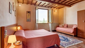 A bedroom with a bed, a sofa, a wooden wardrobe, and a window with a view. - Il Colombaino by Interhome (Florence)