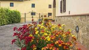 A yellow building with a stone wall, a gate, and a garden with colorful flowers. - Il Colombaino by Interhome (Florence)