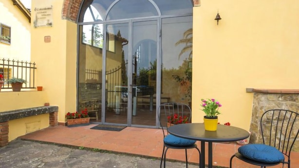 A patio area with a glass door entrance, a round table with two chairs, and potted plants. - Il Colombaino by Interhome (Florence)