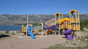 A playground with slides and climbing structures, set against a backdrop of mountains and a clear sky. - Vacation home Dada by Interhome (Rovanjska)