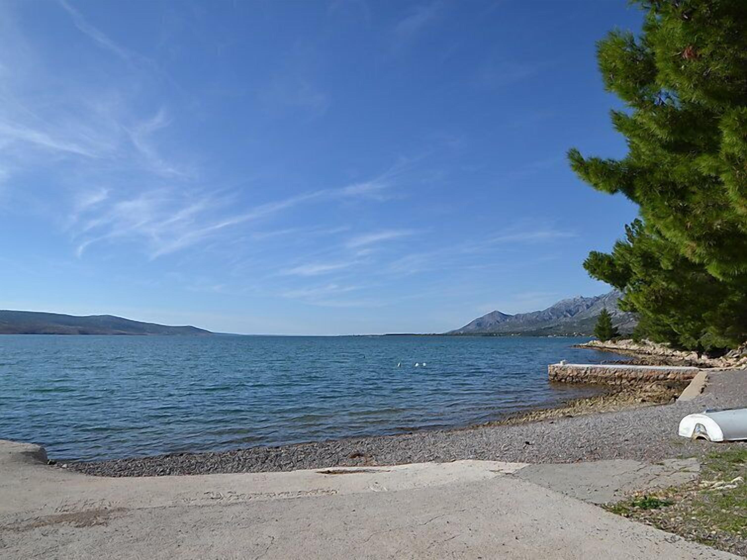En klar vy över en sjö med en stenig strand och ett bergskedja i fjärran, under en blå himmel.