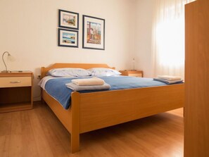 Une chambre à coucher bien rangée, avec un lit en bois, une table de chevet, une commode et deux tableaux encadrés accrochés au mur.