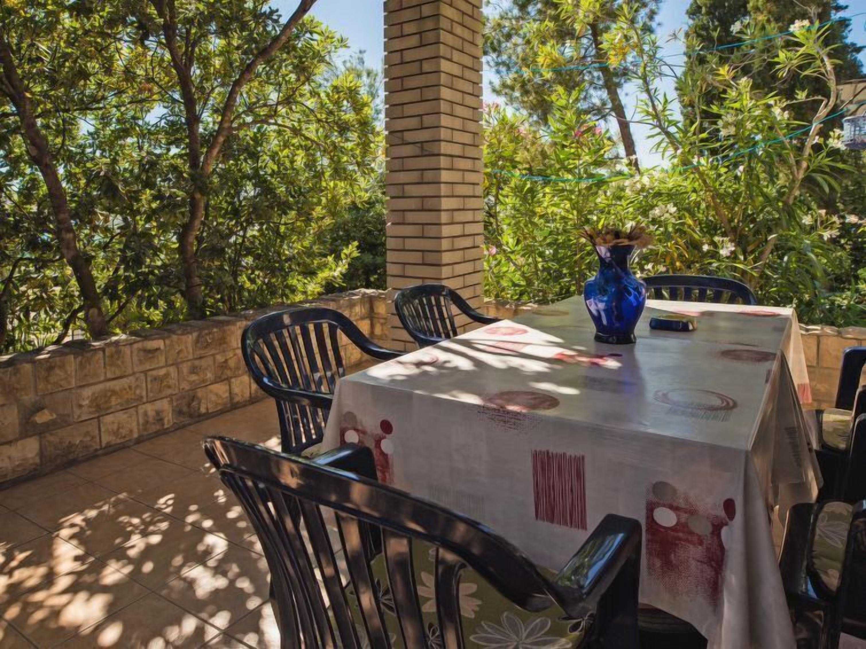 An outdoor patio with a table covered in a tablecloth, surrounded by chairs, and a vase with flowers.