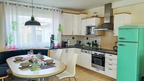 Et moderne køkken med hvide skabe, et grønt køleskab, et spisebord dækket til fire personer, og et vindue med gardiner.