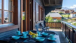 A wooden building with a balcony, a table with blue bowls and a fruit bowl, and a view of houses in the background. - Mustela by Interhome (Nendaz)