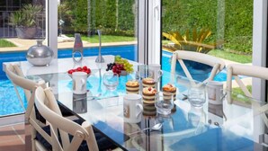 A dining table with a glass top, surrounded by chairs, near a pool with a view of a house and greenery. - Amsterdam by Interhome (St Antoni de Calonge)