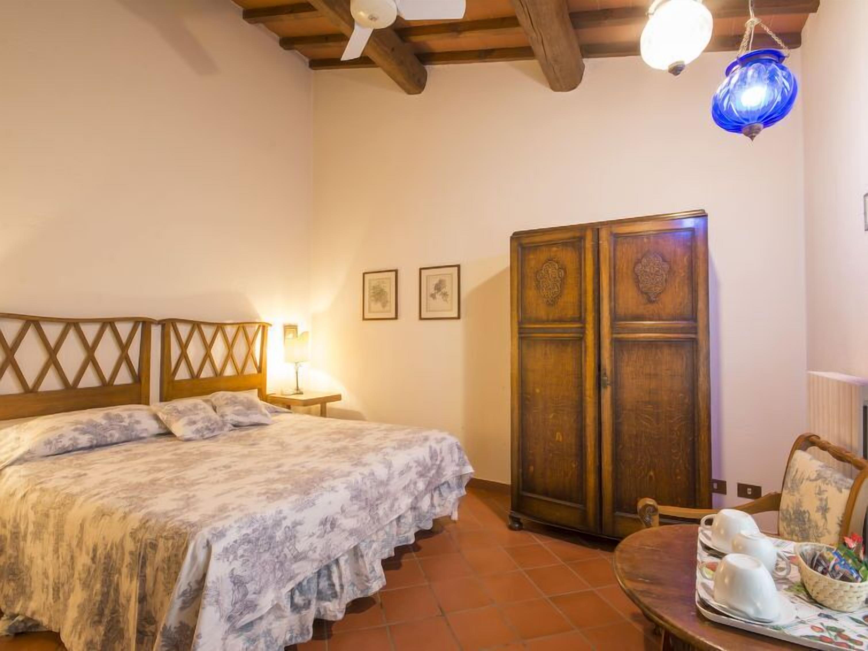 A bedroom with a bed, a nightstand, a wardrobe, and a table with teacups and a basket.