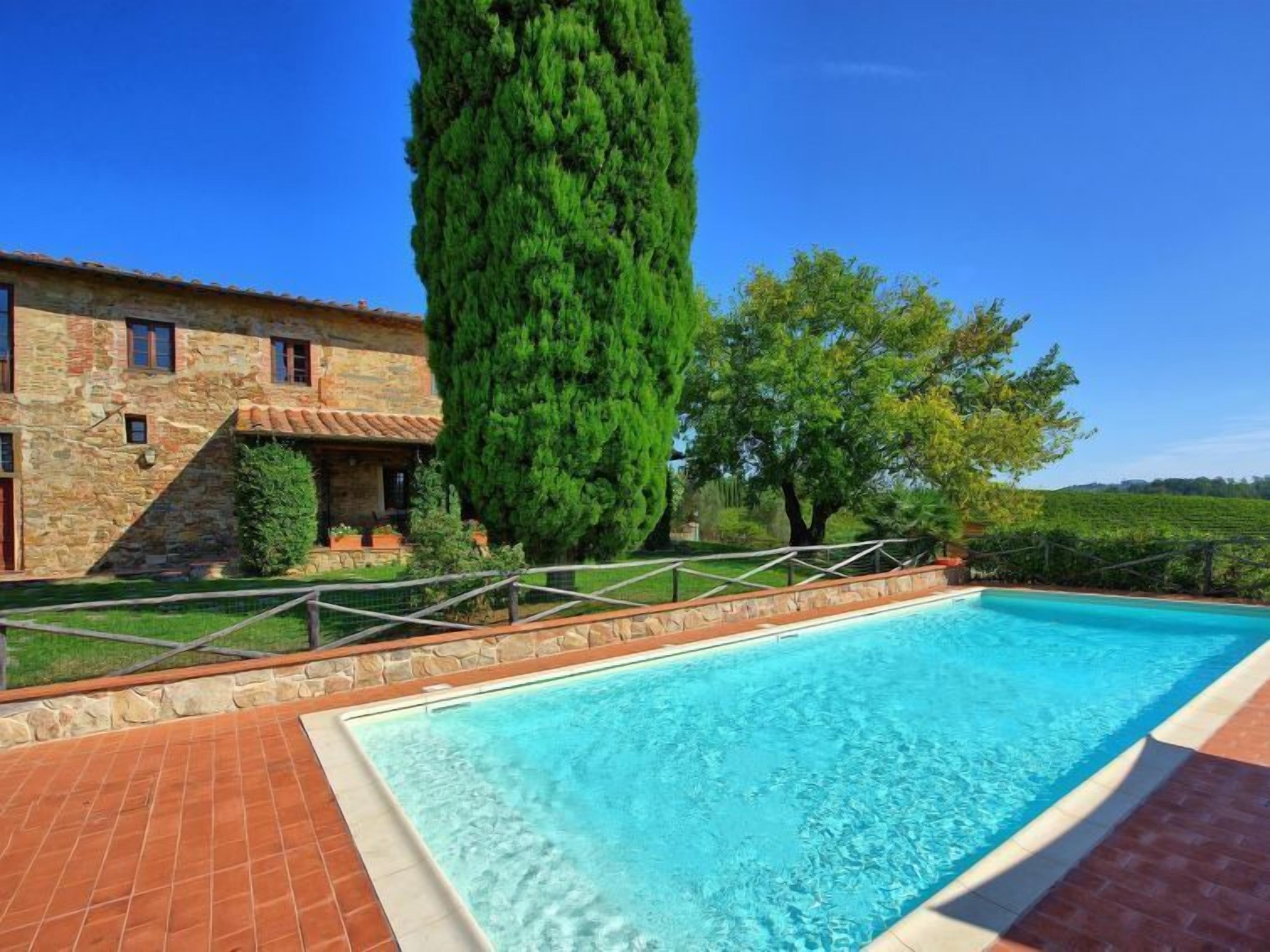 A swimming pool with a stone deck, a stone building with windows, and a tall tree.