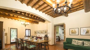 A spacious living area with a wooden ceiling, a dining table set for four, a green sofa, and a coffee table with fruit.