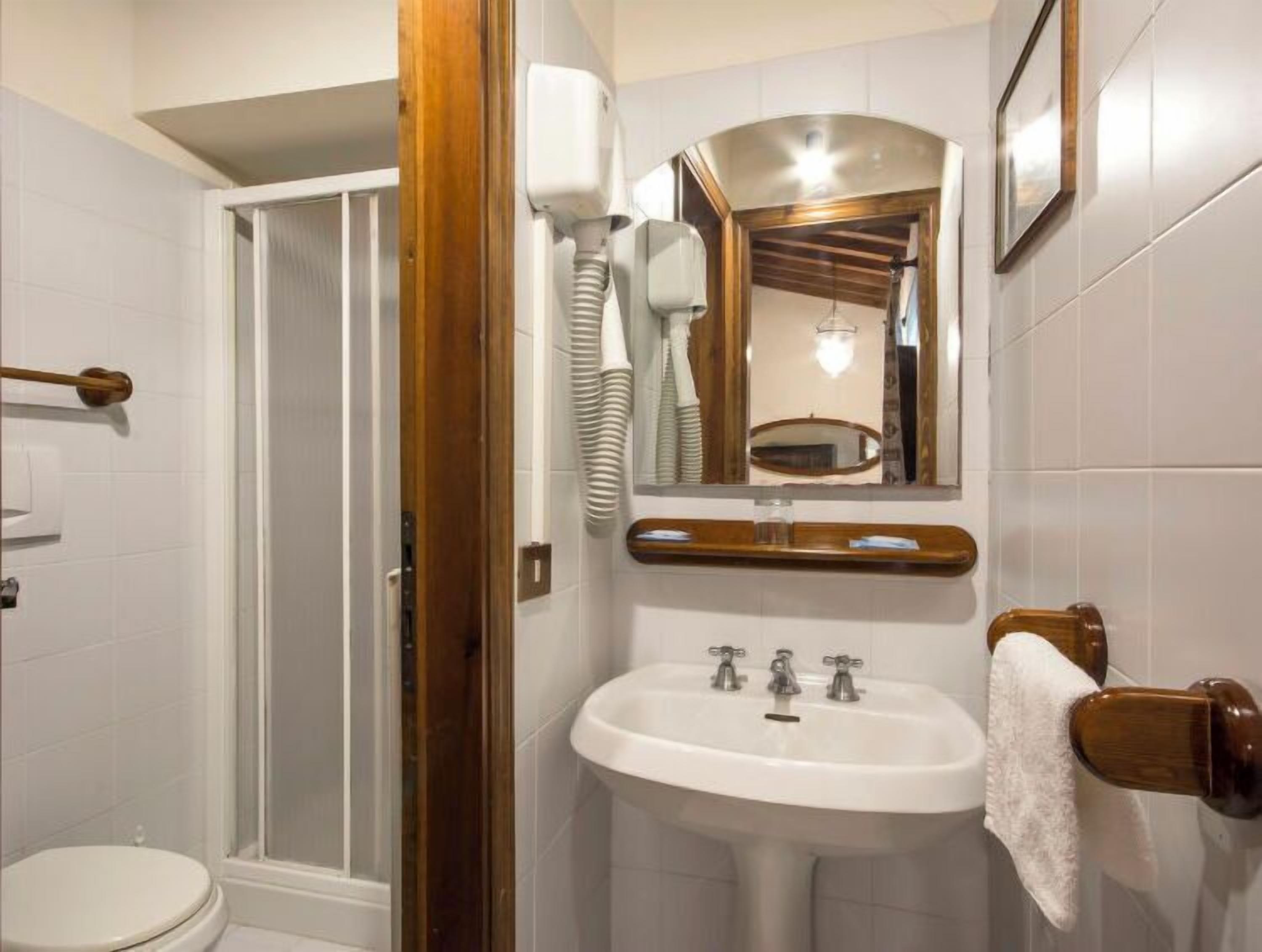 A bathroom with a shower, toilet, sink, and a mirror with a towel rack.