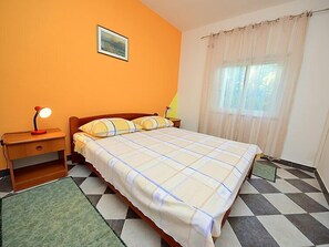 A bedroom with a bed, a nightstand, a lamp, a picture on the wall, and a window with curtains. - Vacation home Katica by Interhome (Trstenik/Dingač)