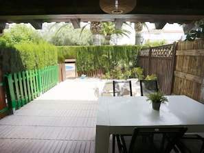 A patio area with a table and chairs, surrounded by a wooden fence and lush greenery.