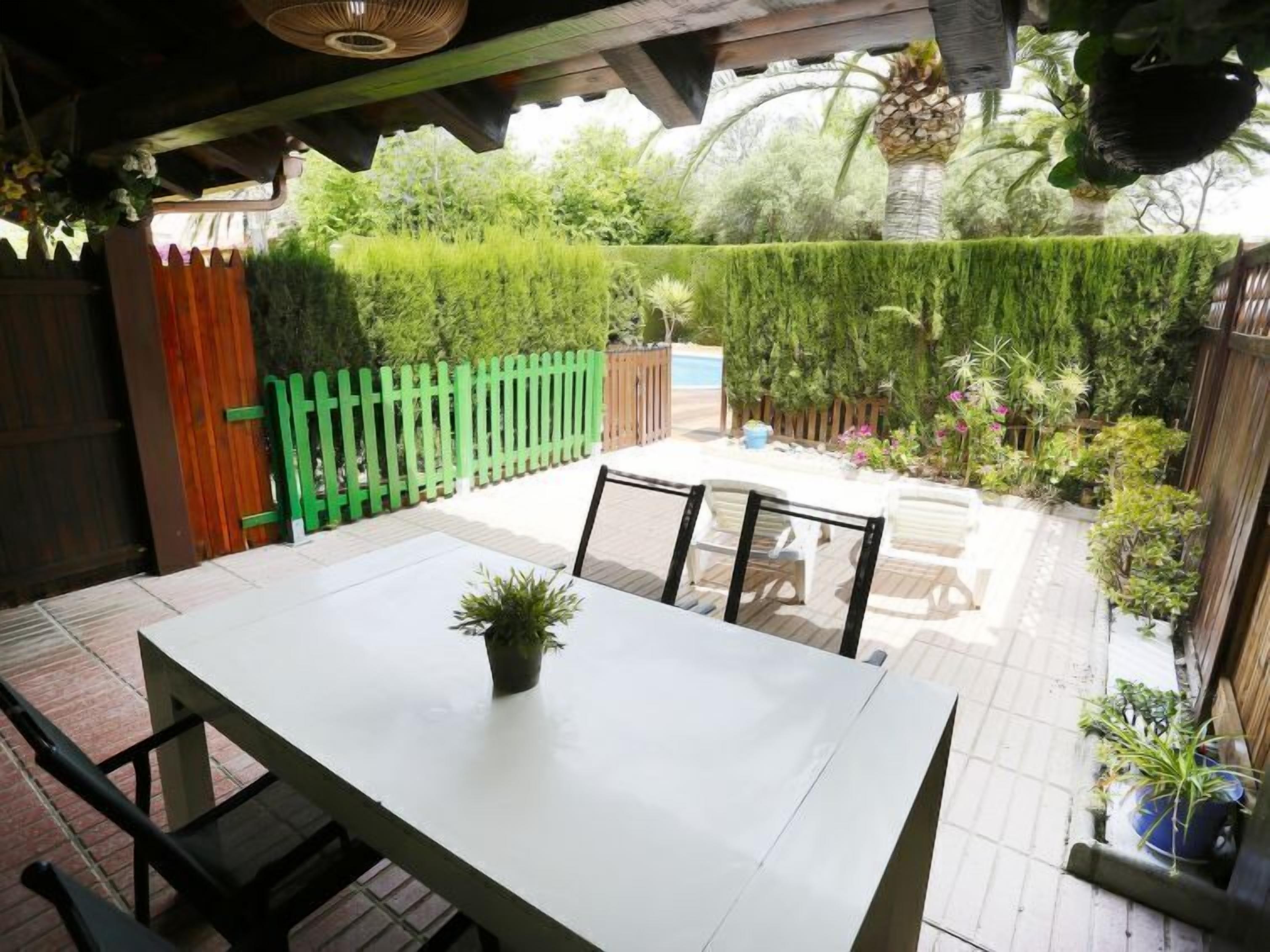 A patio with a table and chairs, surrounded by a wooden fence and various plants.