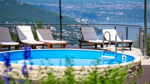 A poolside area with lounge chairs and umbrellas, overlooking a scenic view of a town and mountains. - Apartment Laurus by Interhome (Lovran/Tuliševica)