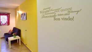 A room with a yellow wall and a welcome sign in multiple languages. There is a small table with a vase of flowers and a dark-colored sofa. - Apartment Laurus by Interhome (Lovran/Tuliševica)