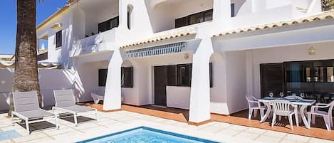 A two-story building with a swimming pool, white walls, and a tiled roof.